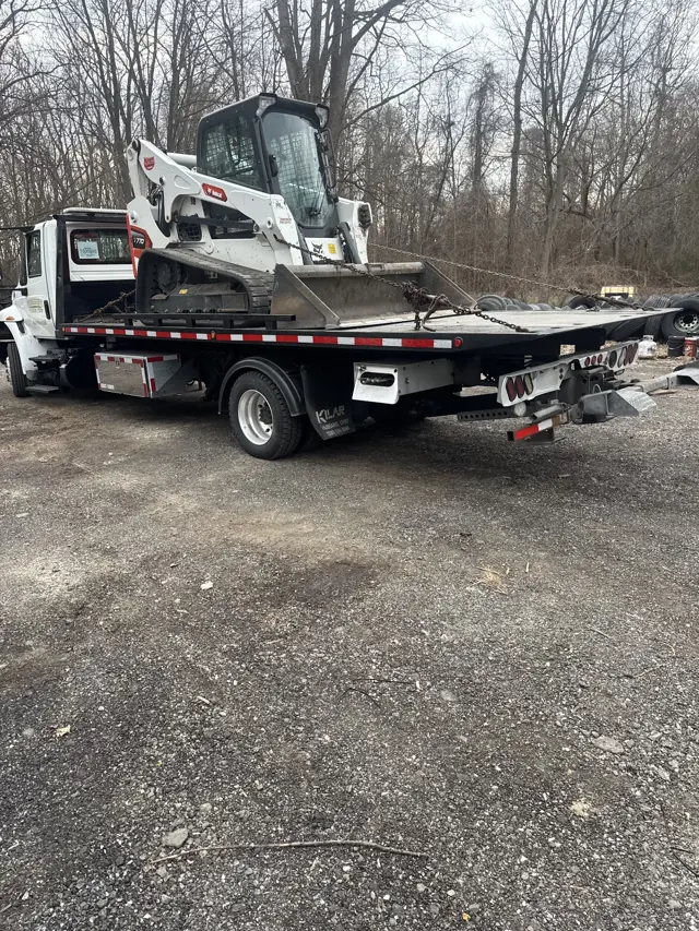 A compact loader pictured on the bed of Progressive Towing and Tire’s truck