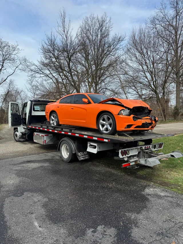 A side view of our white flatbed carrying an orange car with front-end damage