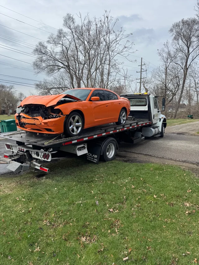 An orange car with front-end damage loaded on our white flatbed truck, photographed from the front of the car